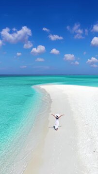 Aerial view of a happy woman in a white dess walking on a beautiful beach with turqouise sea and fine sand in the Maldives islands