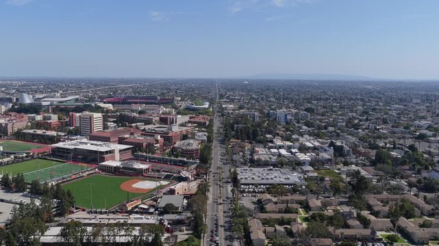 Aerial survey over Los Angeles, California showing university campus with athletics fields, urban residential neighborhoods, cars driving on city streets