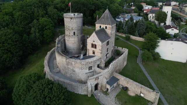 1. Aerial drone pull-back shot of the medieval Bedzin Castle in Poland, revealing a wide city panorama with an industrial power plant on the horizon at sunset.