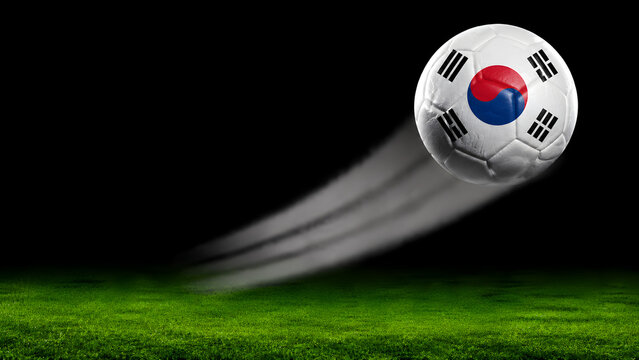 A soccer ball featuring the South Korean flag pattern in motion, leaving a trail against a dark background above a green grass pitch.