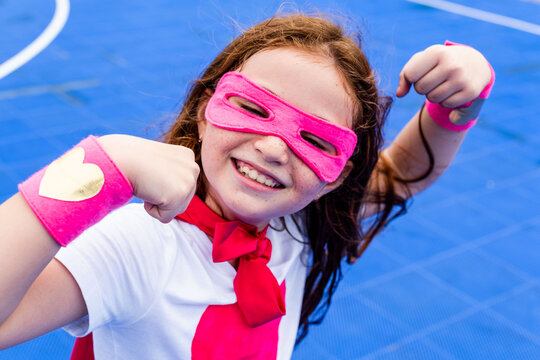 Child in pink superhero costume flexing muscles on blue background.