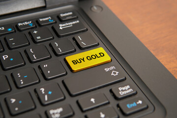 Obraz premium Close up of a computer keyboard with a yellow buy gold key, representing precious metal investment, wealth preservation, financial security, safe haven assets, and long-term investment strategies.