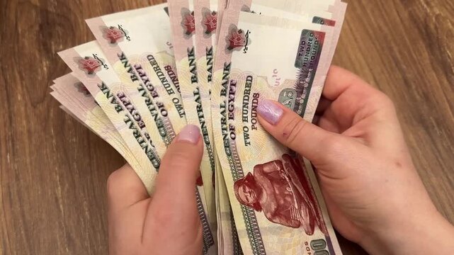 Woman's hands counting a stack of Egyptian banknotes, close-up, fingers flipping paper currency, financial transaction.