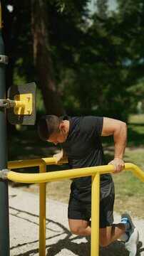 A muscular man performs dips on yellow parallel bars in an outdoor gym. He is focused on his calisthenics workout, demonstrating strength and determination.