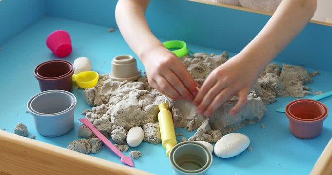 Children activity with kinetic sand for motor and sensory development. Toddler play therapy with colorful toys on wooden sandbox.