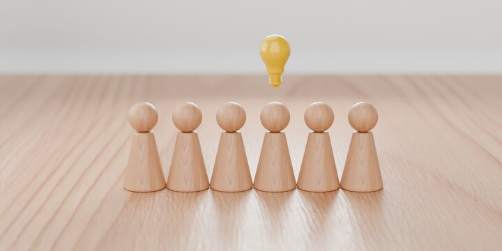 3d wooden pawn figurines in a row with a lightbulb hovering over one one them. Bright idea, innovative thinking