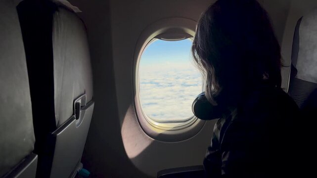 Girl airplane passenger gazes out window at clouds and sky, peaceful flight, travel wonder, childhood curiosity.