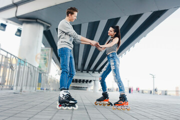 Fototapeta premium Young couple rollerblading together holding hands