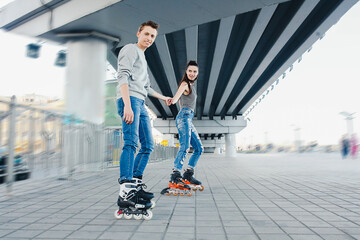 Obraz premium Young couple rollerblading holding hands under bridge