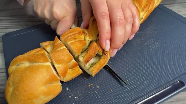 A woman slices a fresh baguette in close-up, knife cutting crispy golden crust in a warm kitchen.