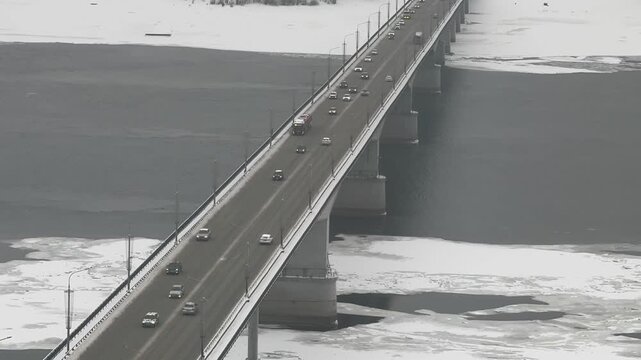 Timelapse of a bridge over a frozen winter river, daytime, slow clouds, drifting ice, city traffic.