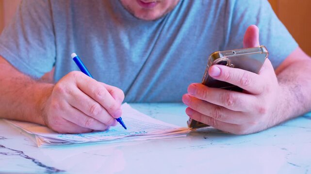 Low angle close-up of man holding a smartphone and filling out form with a marker. Shallow DoF, natural light. Metaphor for mobile banking, two-factor authentication, online tax filing and remote work