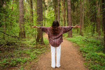 Obraz premium Pregnant woman relaxing in a forest, standing on a dirt path with arms extended, embodying freedom and connection to the environment, enjoying a healthy pregnancy outdoors