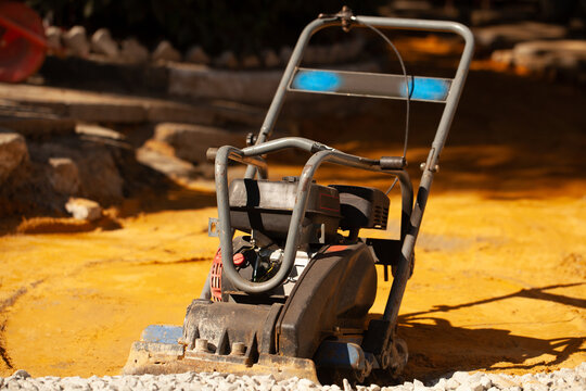 Construction equipment is ready for use at a building site in the afternoon with yellow ground and stone path