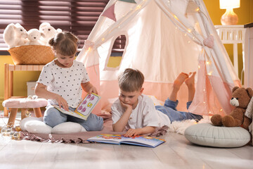 Little girl and boy reading books near wigwam at home © New Africa