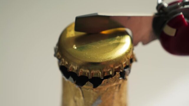 Close-up of opening glass bottle with corkscrew opener. Macro shot of metal crown cap being removed from beverage bottle on white background. Beer, soda or lemonade bottle opening concept. High