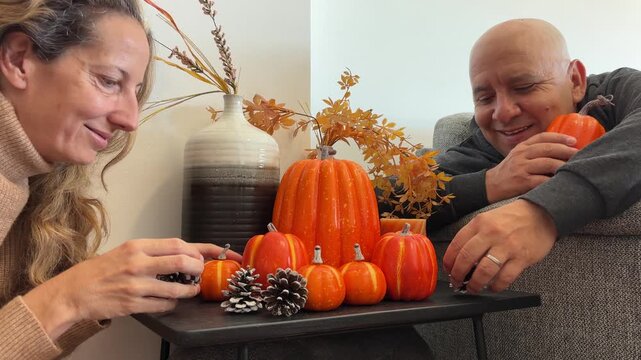 Pareja decorando mesita con calabazas y pi&ntilde;as oto&ntilde;ales