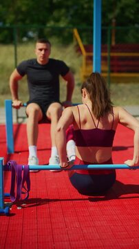A fit performs triceps dips on parallel bars at an outdoor sports ground. They engage in a focused workout, building strength and fitness together.