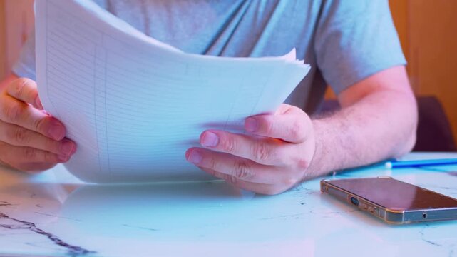 Low angle close-up of hands holding and flipping through a stack of documents. Blurred silhouette in home office. Shallow DoF, natural light. Metaphor for document review, remote work and auditing.