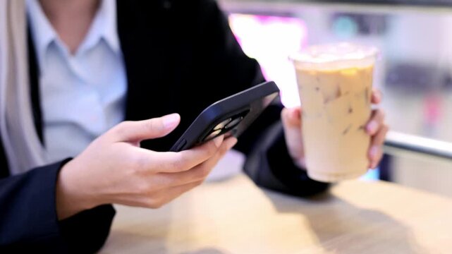 Person holding smartphone and iced coffee cup casual business attire, enjoying beverage refreshment and technology relaxed indoor setting with mobile phone and hand for modern lifestyle drink