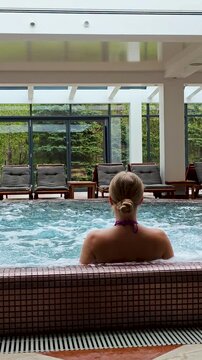4K spa vertical video footage of blonde woman relaxing in jacuzzi hot tub, luxury wellness spa, serene wellness lifestyle, beauty relaxation, indoor spa atmosphere.