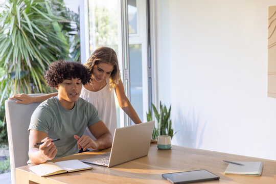 Couple collaborating on silver laptop at home workspace by sliding glass door with plants