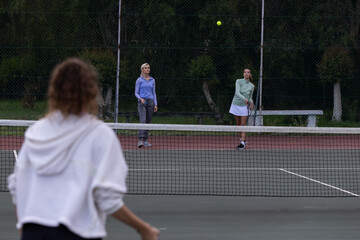 Obraz premium Female friends playing tennis at park, wearing hoodie and tennis skirt, hitting ball with rackets