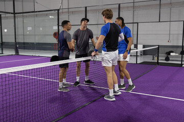 Obraz premium Diverse male players wearing sportswear shaking hands at purple racket court by net and bags