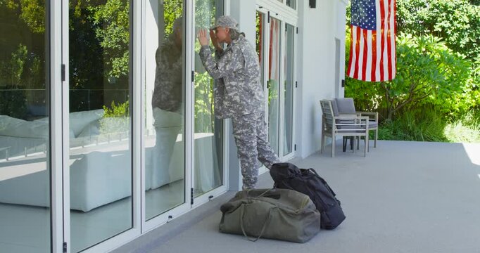 Adult female in camo arriving on patio with duffel bags, leaning on glass, peering for family