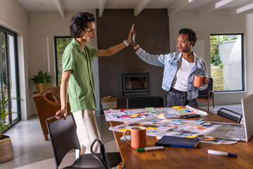 Obraz premium Diverse coworkers high-fiving at wooden table in open living room with denim jacket, sticky notes