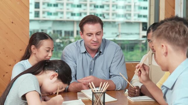 Smart high school boy in casual shirt asking professional teacher while student with mixed races writing book. Caucasian instructor giving comment while creative child pointing at note. Edification