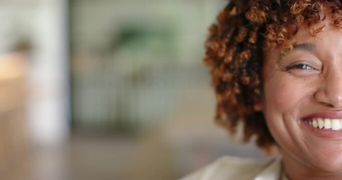 African American woman 30s smiling, responding to camera shifts, blouse, table, plant, copy space