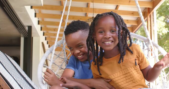 Two African children sitting in white macrame chair on porch, responding to caller, laughing