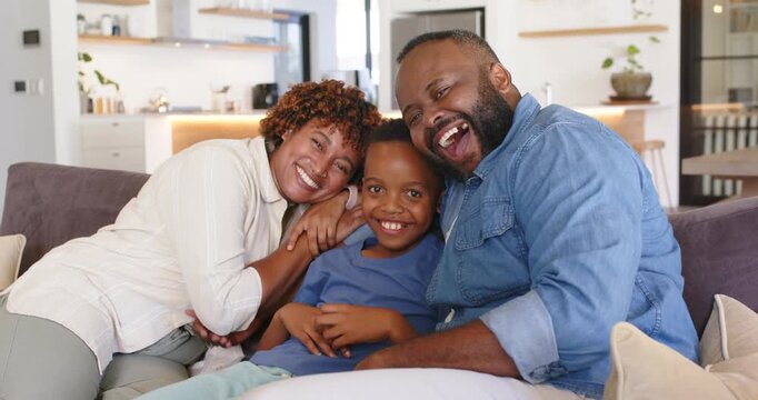 African American family responding to camera, leaning, hugging, resting heads on sofa and laughing