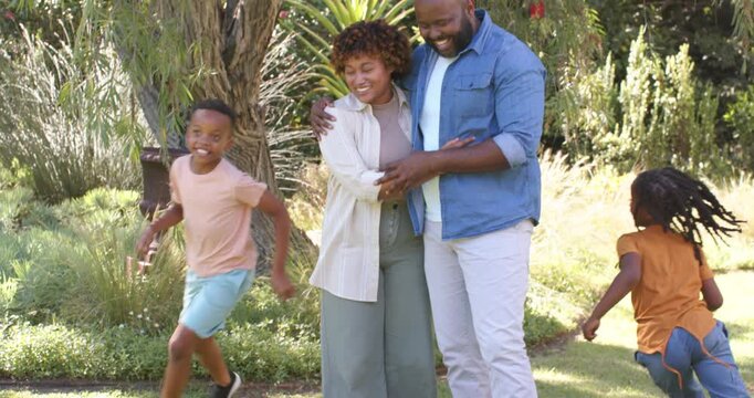 African American couple hugging near tree as kids dashing, making them laugh and hug more