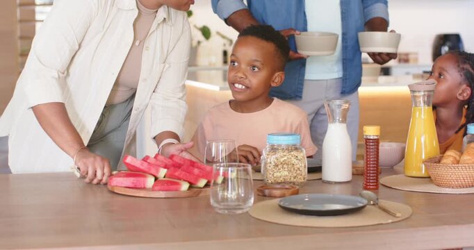 African American family making breakfast at island, woman placing watermelon, father handing bowls
