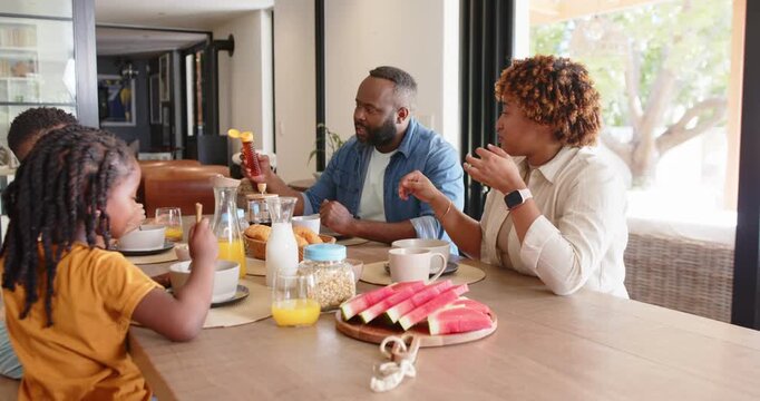 African American family at table while father testing squeeze bottle and pouring, helping child eat
