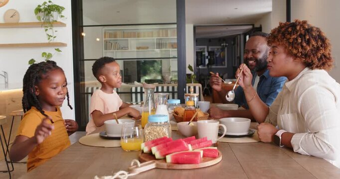 Family of four reacting to daughter's pointing while having breakfast at home with watermelon