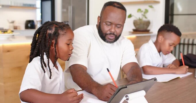 African American dad teaching two boys at kitchen table, pointing tablet while left child speaking