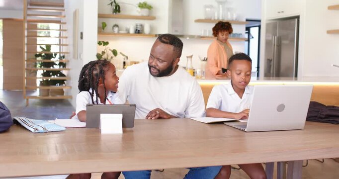 African American family at table dad pointing to tablet stand helping girl study son typing laptop