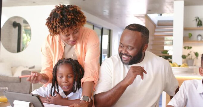 African American family mom urging daughter reading with tablet for homework as father guiding son