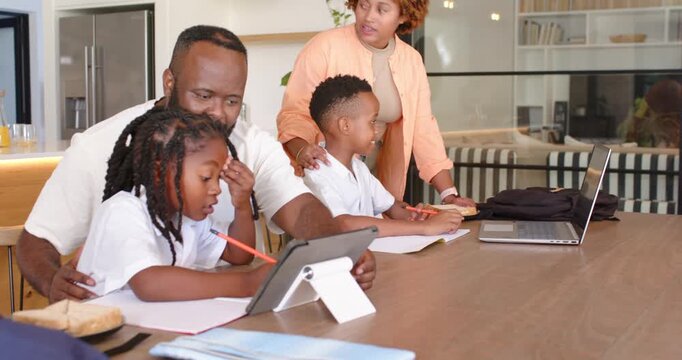 African American family doing homework at kitchen table, father guiding daughter using tablet