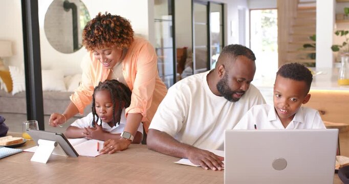African American family guiding children with schoolwork at home using tablet and laptop