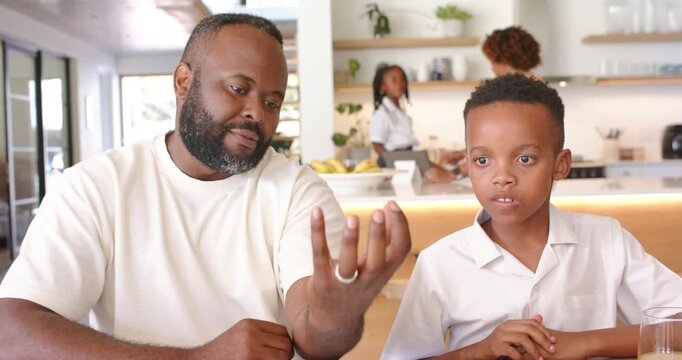 African American father and son sitting at table teaching math and placing green bead boy watching