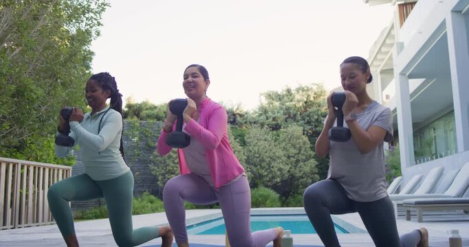 Diverse women in leggings following center cue, lunging with goblet weights on mats beside pool