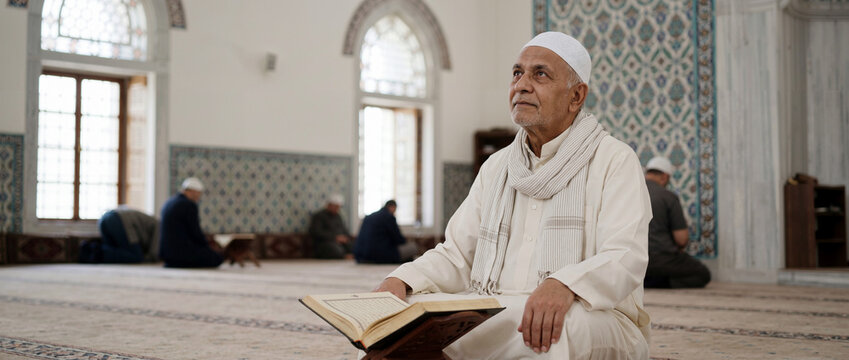 Older Muslim man reading the Quran in a mosque. Senior male worshipper in traditional clothing sitting on the floor during prayer
