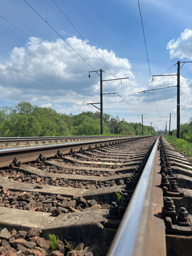 Railway tracks with electric power lines stretching into distance under blue cloudy sky