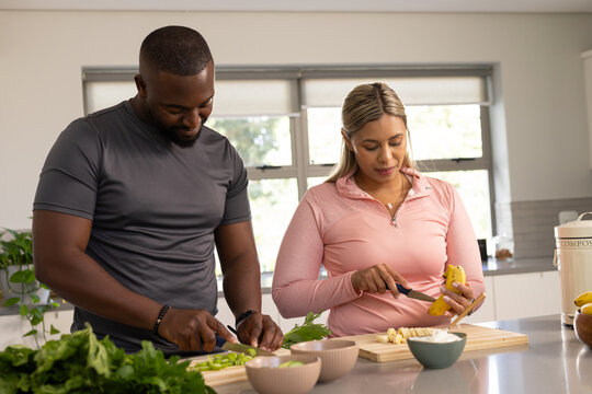 African American couple in athleisure preparing salad on boards at counter with compost bin