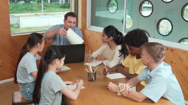 Caucasian teacher and smart boy discuss about project at classroom. Professional instructor talking about classwork while giving a paper to high school child with diverse student listen. Edification