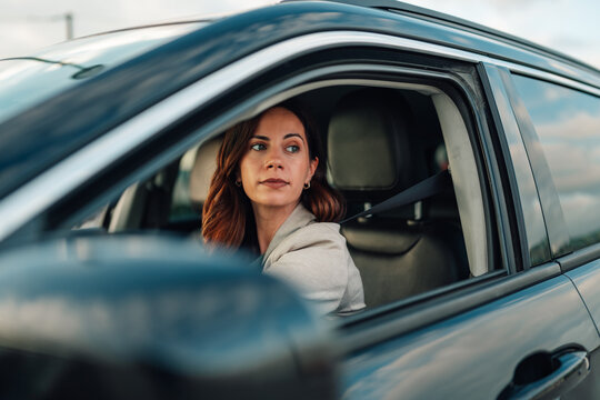Woman looking back while driving a car, wearing a seatbelt, focusing on parking or reversing maneuvers